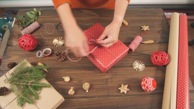 Christmas flat lay of unready hand crafted gift box on rustic wooden table with rolls of craft and colour wrapping paper, pine cones, fir branches and decor elements.