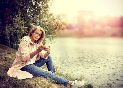 Pretty blonde woman walk in the park and look at smartphone