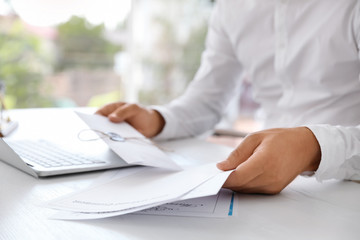 Male notary with documents and laptop at table in office, closeup