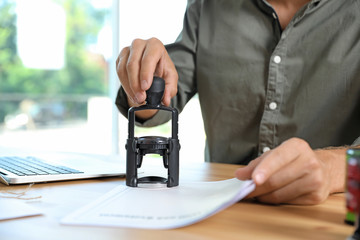 Male notary stamping document at table in office, closeup - obrazy, fototapety, plakaty