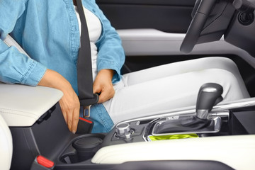 Female driver fastening safety belt in car, closeup
