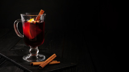 closeup glass of mulled wine with orange and cinnamon on dark black background, place for text