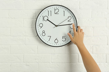 Woman touching clock on white brick wall. Time management