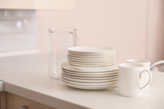 Stack of clean dishes, cups and glass jug on table in kitchen