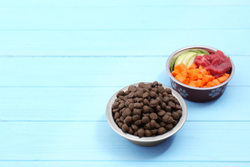 Bowls with dry and natural dog food on wooden background. Space for text
