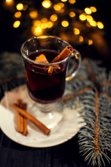 mulled wine on  white plate on black wooden table, cinnamon sticks and orange, christmas tree and lights, top view