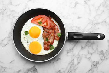 Fried sunny side up eggs with tomato and bacon in pan on marble background, top view