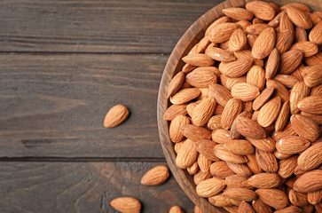 Tasty organic almond nuts in bowl and space for text on table, top view