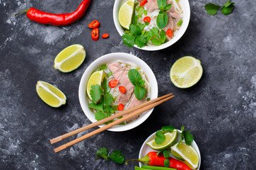 Traditional Vietnamese Soup Pho Bo with Rice Noodles, Beef and Herbs on Dark Background
