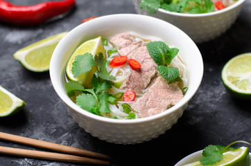 Traditional Vietnamese Soup Pho Bo with Rice Noodles, Beef and Herbs on Dark Background