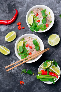 Traditional Vietnamese Soup Pho Bo with Rice Noodles, Beef and Herbs on Dark Background