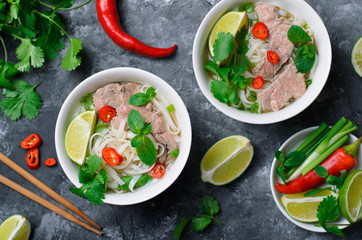 Traditional Vietnamese Soup Pho Bo with Rice Noodles, Beef and Herbs on Dark Background
