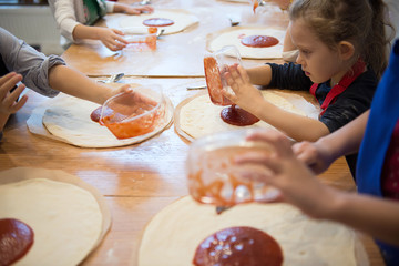 Children's hands make pizza - spread tomato sauce on the base.