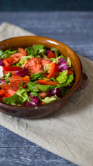Fresh salad with tomatoes, mixed greens (arugula, mesclun, mashe) on wooden background top view.  Healthy food. Homemade food, vegetarian diet, vitamin snack (vertically)
