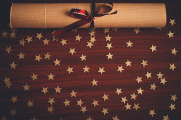 Scroll of paper with brown ribbon and lots of small gold star confetti on the wooden table top view flat lay