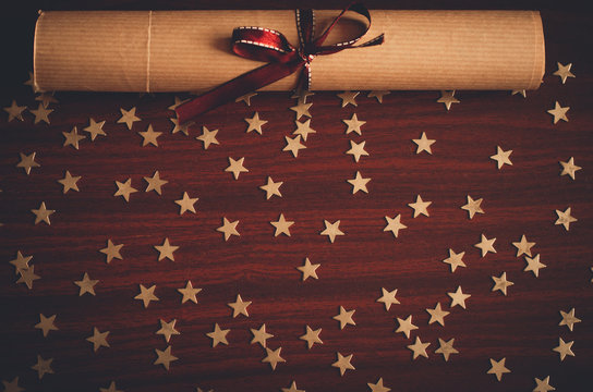 Scroll of paper with brown ribbon and lots of small gold star confetti on the wooden table top view flat lay