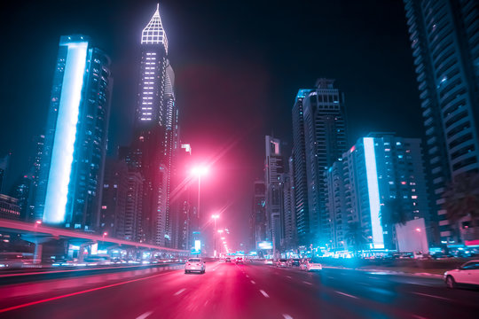 Driving a car on Sheikh Zayed Rd in Dubai at night, United Arab Emirates. Blurred motion. Duotone retro wave neon noir lights color toned