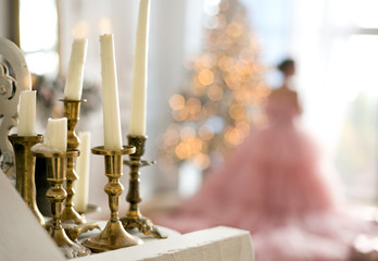 Silhouette of a girl in a beautiful pink dress near the Christmas tree. Candles in the foreground