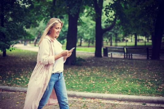 Pretty blonde woman walk in the park and look at smartphone
