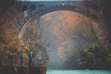 Man standing under old bridge in autumn landscape. Vintgar, Slovenia