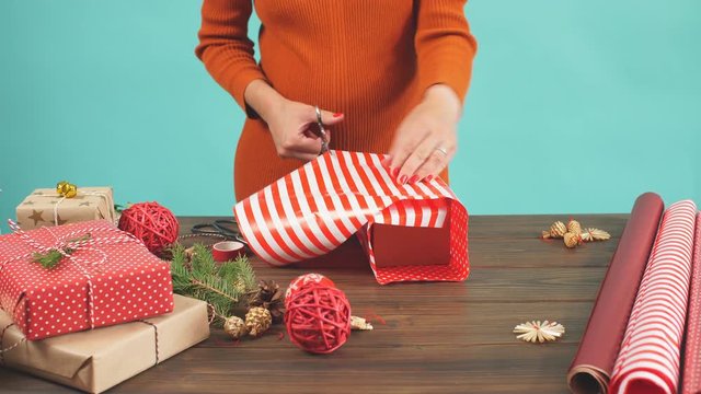 Christmas flat lay of unready hand crafted gift box on rustic wooden table with rolls of craft and colour wrapping paper, pine cones, fir branches and decor elements.