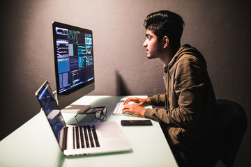 Indian Male programmer working on desktop computer at white desk in office.