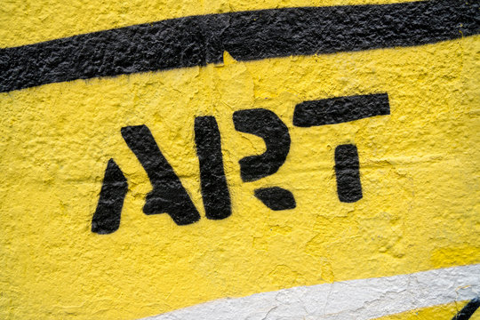 Fragment of graffiti drawing. Word &ldquo;art&rdquo; in black on yellow old wall decorated with paint in street art style.
