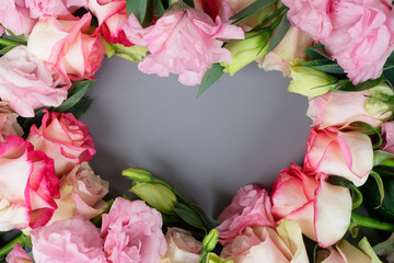 Rose fresh flowers on gray table from above, flat lay frame in shape of heart with copy space