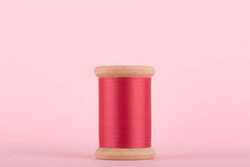 Pink Thread, Cerise Pink Wooden Thread Bobbin isolated on Pastel Pink Background, Copy Space, centered.