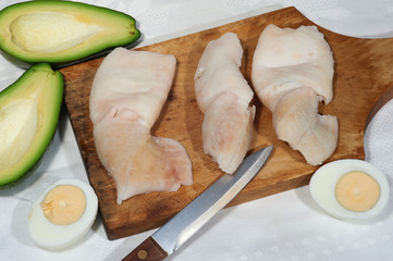 Three calamares, avocado, eggs and knife on cutting board on white napkin