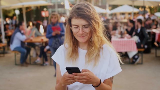 Happy and excited amused teenager or millennial hipster from generation Z uses smartphone technology, looks up at camera and gently smiles with natural beautiful smile, confident and cute