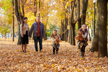 Happy family is in autumn city park. Children and parents running with leaves.. They posing, smiling, playing and having fun. Bright yellow trees.
