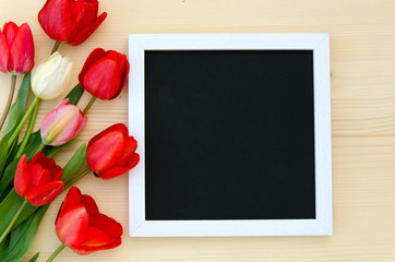 Tulips with blank black chalkboard picture frame on a light wooden background