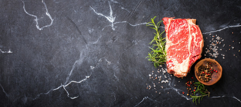 Raw Fresh Marbled Meat Beef Steak. Herbs and Seasonings on a black marble   Background Rosemary Pepper and Salt Ingredients for Cooking Top View Copy space for Text