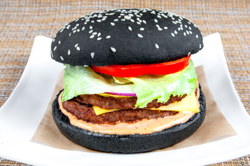 Classic hamburger with black bread and fresh vegetables on a white plate.