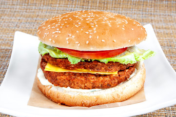 Classic hamburger with black bread and fresh vegetables on a white plate.