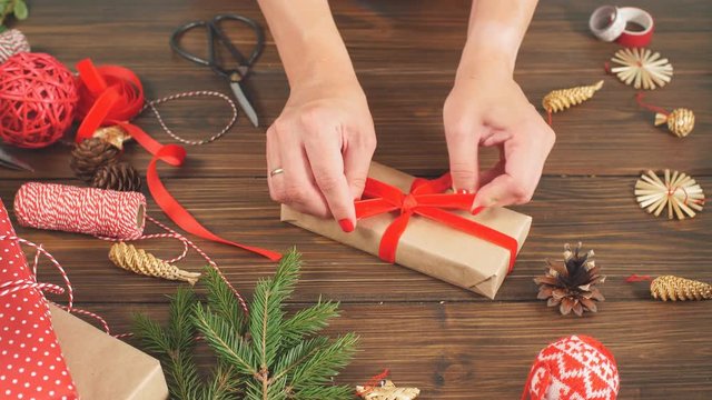 Christmas flat lay of unready hand crafted gift box on rustic wooden table with rolls of craft and colour wrapping paper, pine cones, fir branches and decor elements.