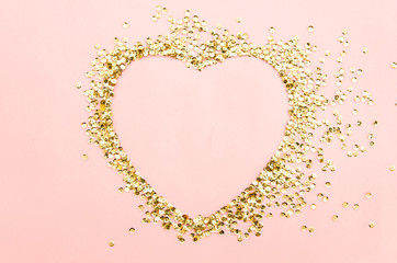 golden sequins shining paillettes heart shapeep on a pink paper background. Template for card, invitation. Blank space for text. Valentines day flat lay mockup.