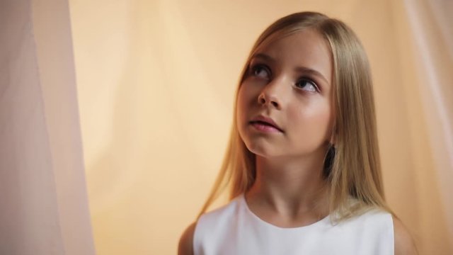 Portrait little girl with a make-up turns his head and looks to the camera talk angry sad serious stand indoors cute young attractive blonde hair beautiful caucasian female pretty slow motion