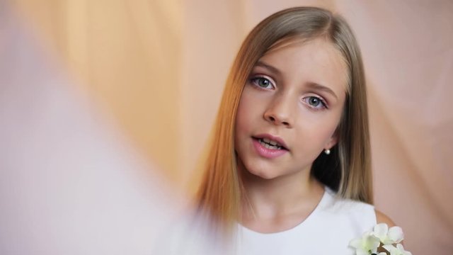 Face little girl with a make-up turns his head and looks at camera talk speak stand indoors cute young attractive blonde hair beautiful caucasian female pretty close up portrait slow motion