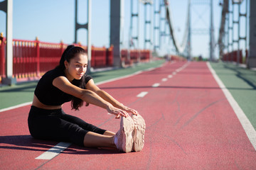 Smiling runner woman doing stretching before jogging at the bridge. Space for text
