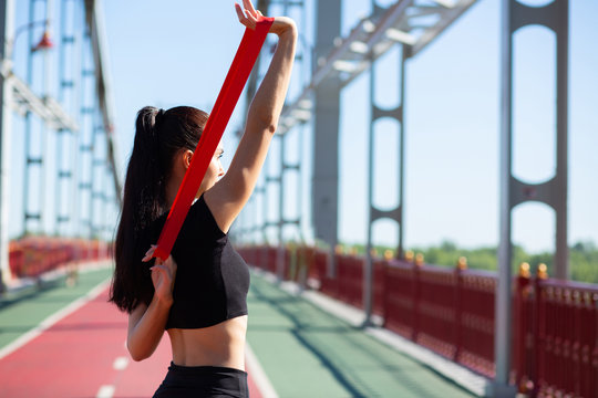 Beautiful Sporty Girl Doing Training With Rubber Resistance Band On A Bridge. Empty Space