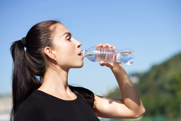 Attractive sporty model drinking water during running at the park in sunny morning. Empty space