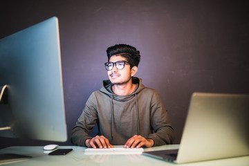 Young indian man programming code on computers screen at desk in dark office
