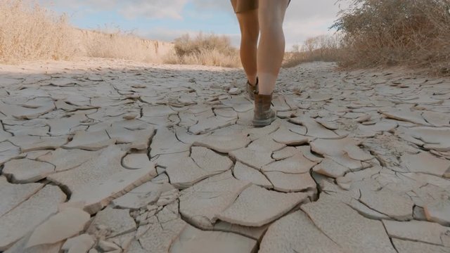 Young woman, female traveller embarks on new adventure walks dry desert land or path in hot country or sahara. Global warming and climate change effects. Drastic danger for environment