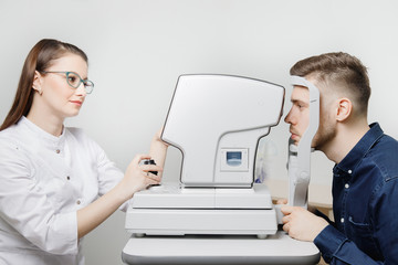 Attractive dark-haired young woman doctor measures eye pressure on ophthalmic equipment to...