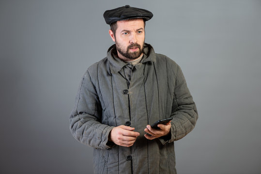 Peasant 35 years dressed in old-fashioned clothes with smartphone in hand, serious and concentrated view, studio shot. Concept - village dweller and modern technology