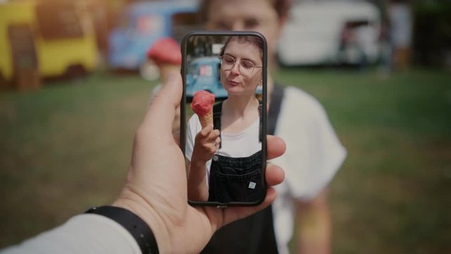 Cinemagraph of cute funny looking girl or young hipster millennial teenager woman eat ice cream or gelato, when best friend makes video for social media on smartphone. technology is fun