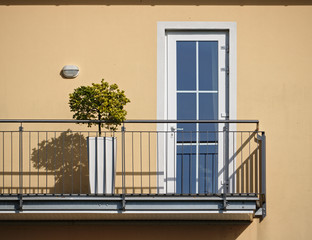 Sunlit beige wall and balcony with bonsai tree and railing casting hard shadows