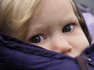 Blond caucasian baby girl with gray eyes in winter jacket looking at camera